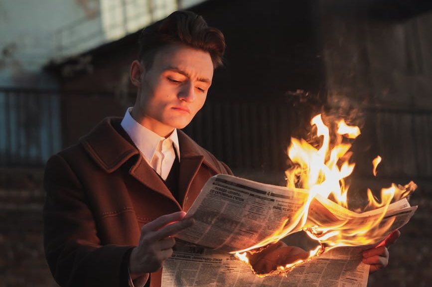 man reading burning newspaper
